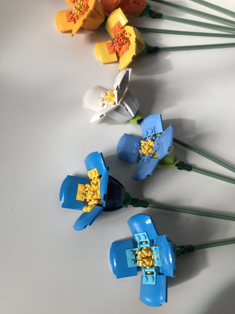 Poppy design by LEGO in alternate color variations: azure, white, medium blue, bright light orange, lying on a white surface