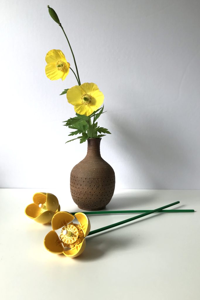 Yellow Welsh Poppy flowers from my garden in a ceramic vase, next to yellow brick-built Welsh Poppies from LEGO's Wildflower Bouquet set, lying on a white desk.