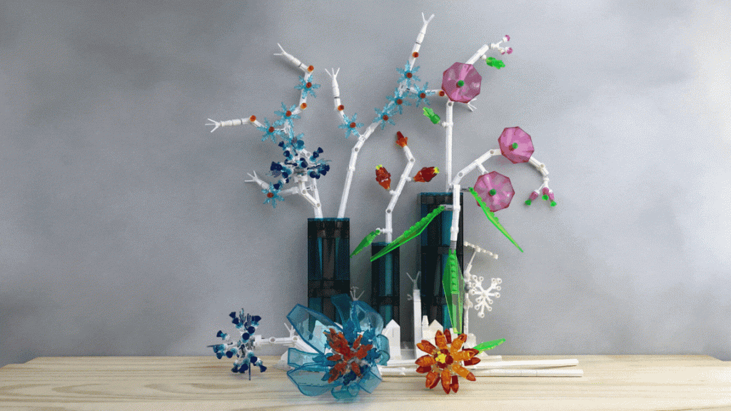 Lego brick-built flowers made from transparent parts and white stems are arranged in three vases. The vases sit in a snowy landscape that hinges to form a different arrangement. Minifigs and a small white dog amid rabbits are added.