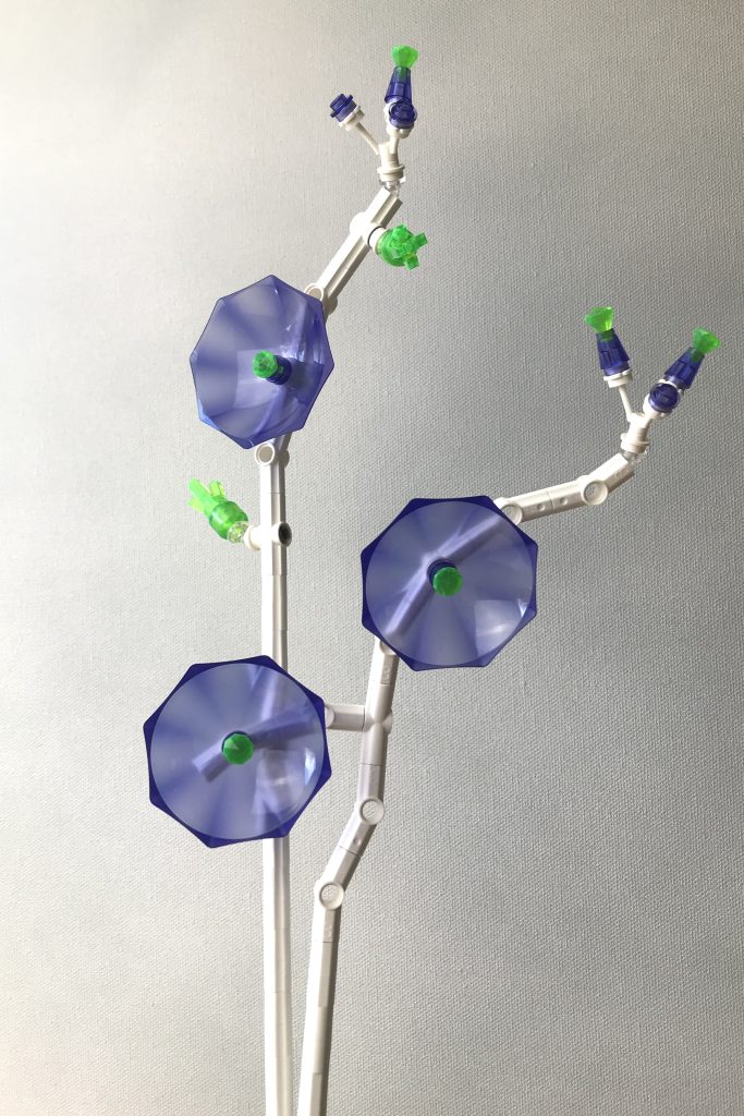 LEGO brick-built flowers MOC with white technic stems, transparent purple umbrellas as flowers, with transparent bright green gem centers, along with purple buds and green clusters of new leaves, on a light gray background.