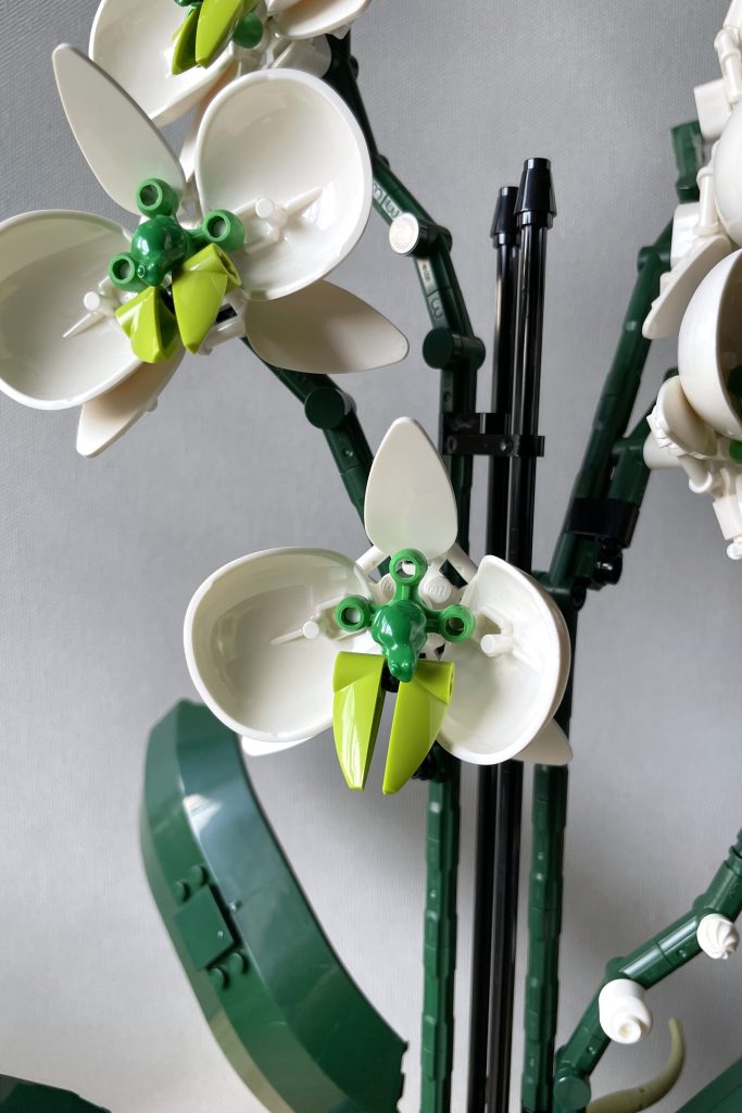 Closeup of a MOC LEGO orchid with white and green flowers, in front of a light gray background.
