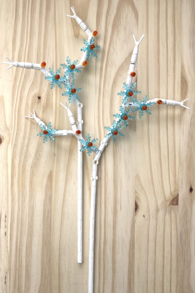 Sprays of transparent light blue and orange LEGO snowflake flowers lying on a light wood surface.